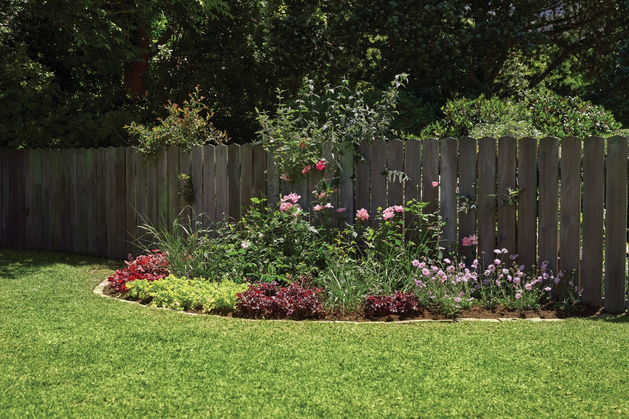 Flowerbed beside a garden fence, separated from the lawn by DIY stone edging