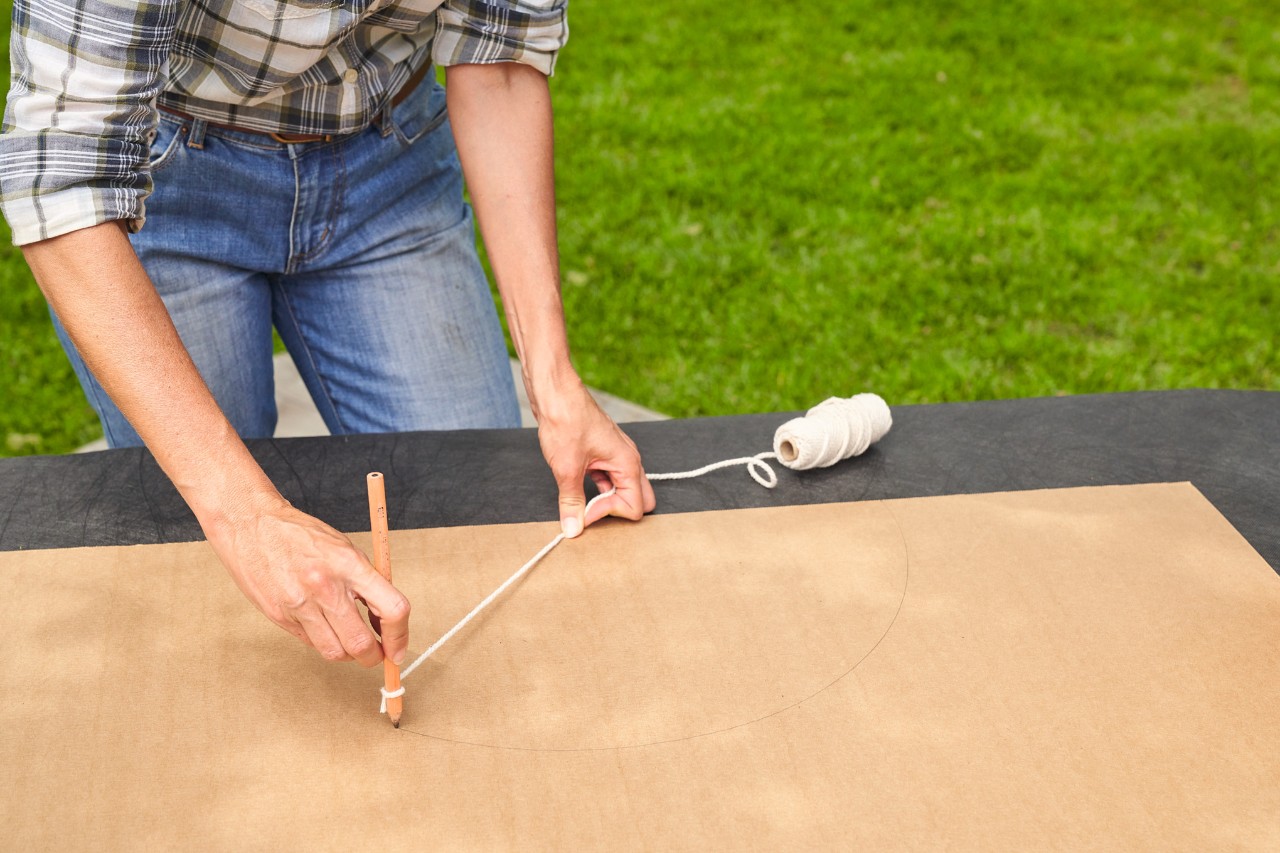 A woman using string and a pen to make a cardboard template for shaping a boxwood bush