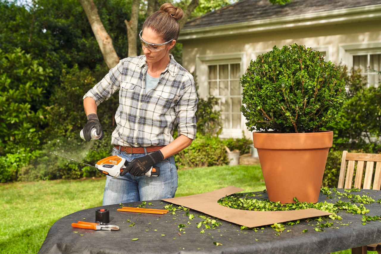 A woman spraying STIHL HSA 26 cordless shrub shears with STIHL Superclean lubricant to clean them after shaping topiary