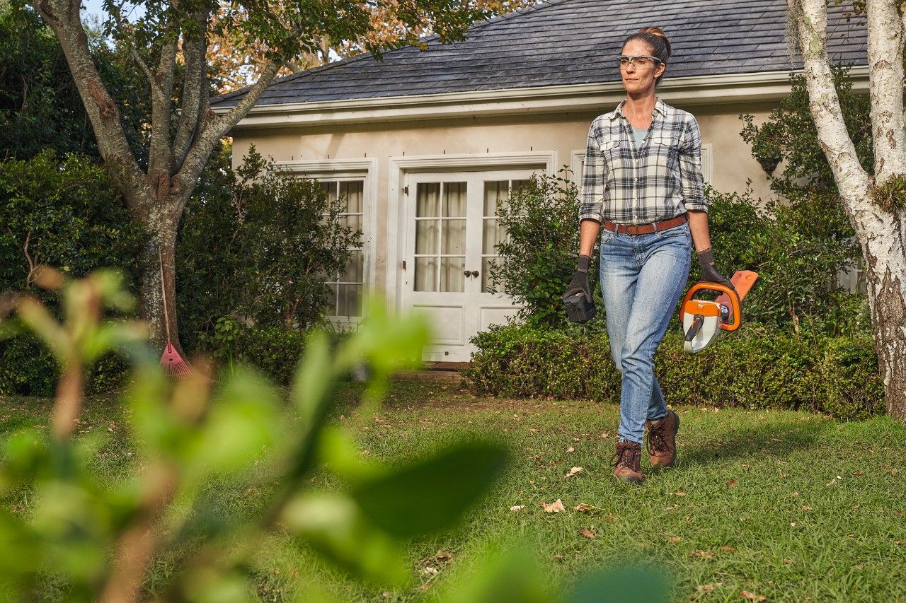 Woman walking through a garden with a STIHL cordless hedge trimmer in her hand
