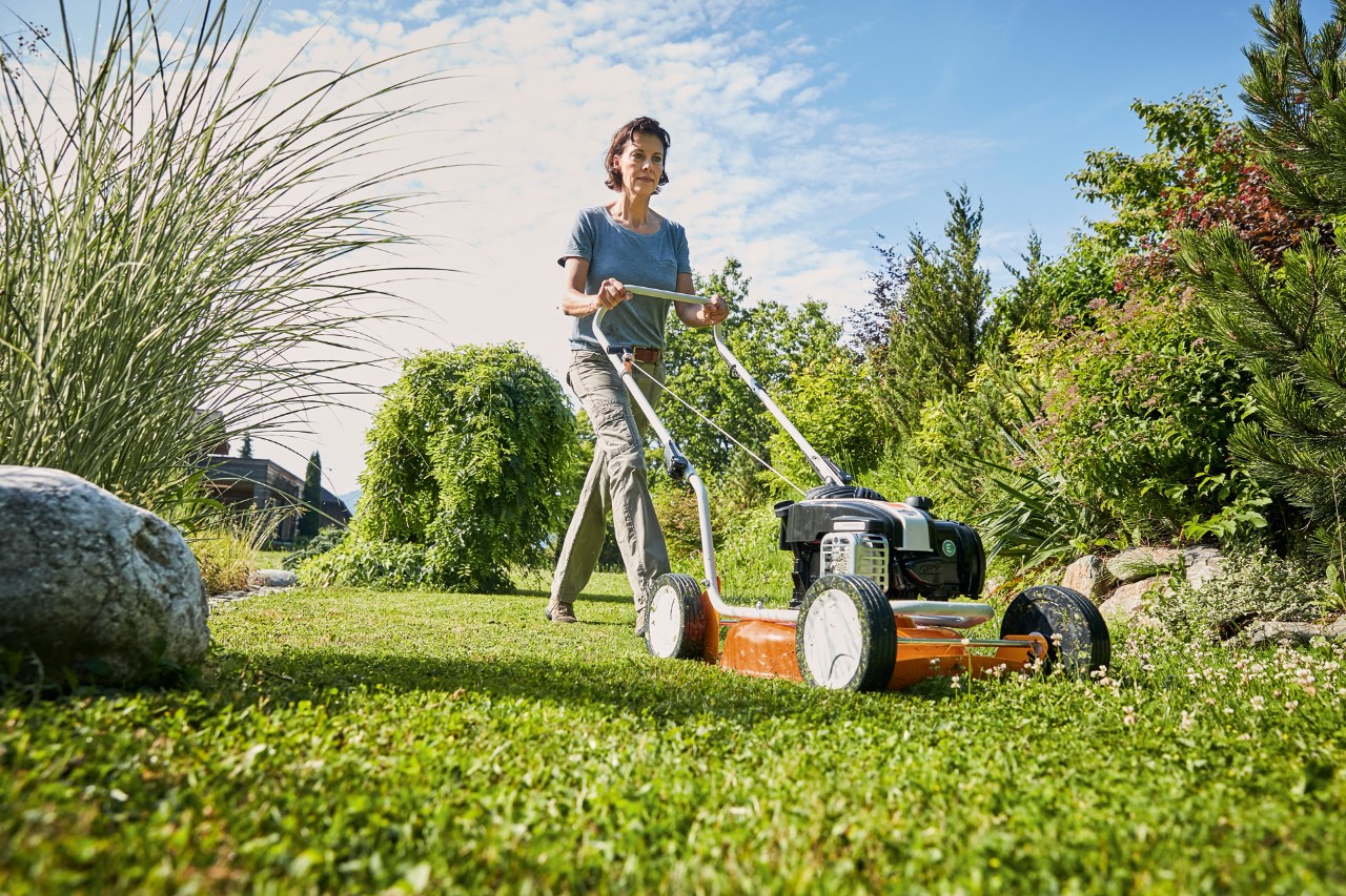 A woman using a STIHL RM 2 R petrol mulching lawn mower on a green piece of land