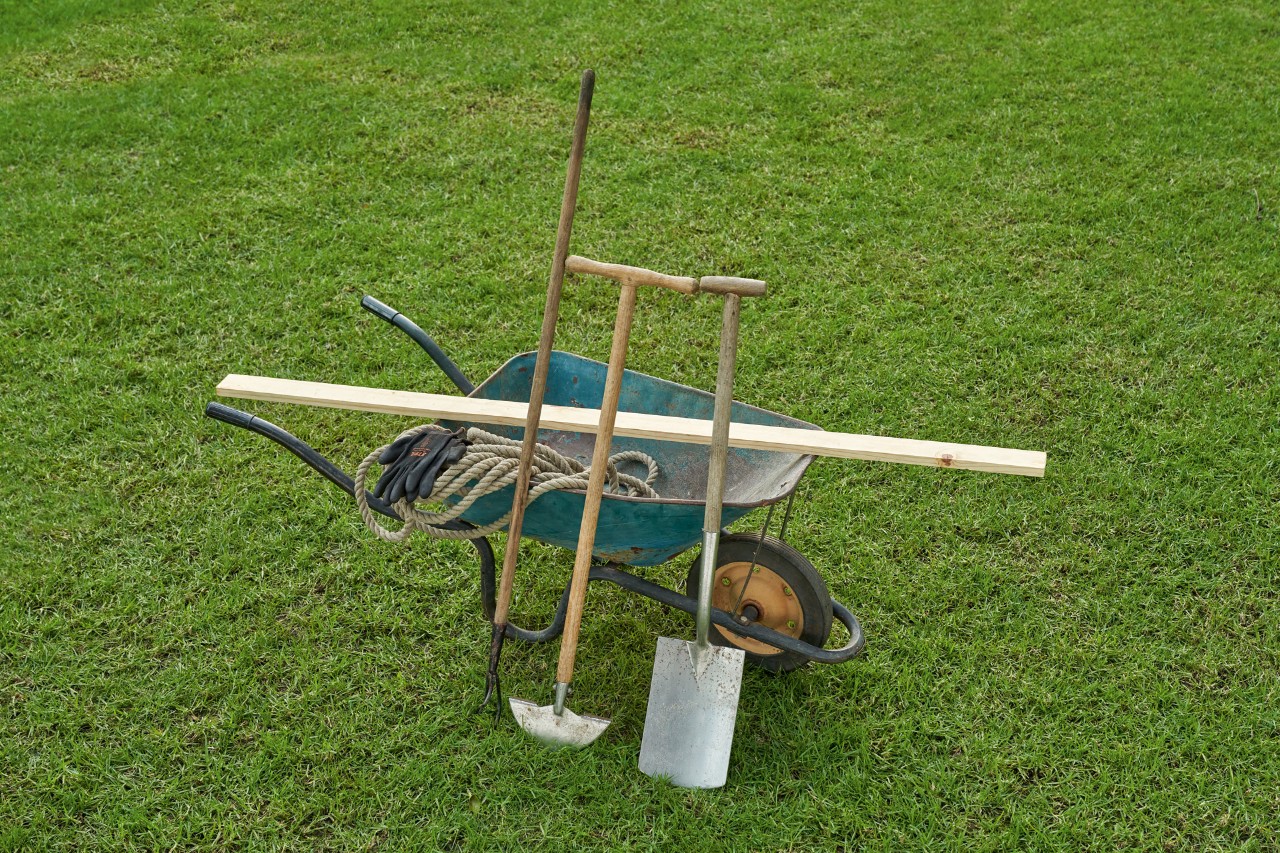 Close-up photo: tool for creating an English-style lawn edge: Wheelbarrow, spade, half-moon edger, rake, garden hose