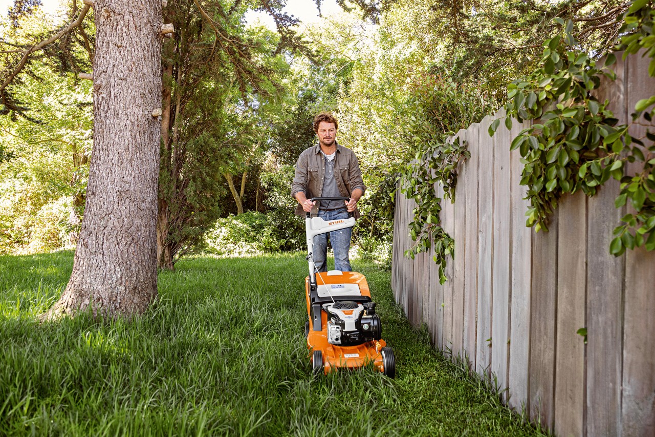 A man mowing the lawn with a STIHL RM 448 TC petrol-driven lawn mower next to a wooden fence