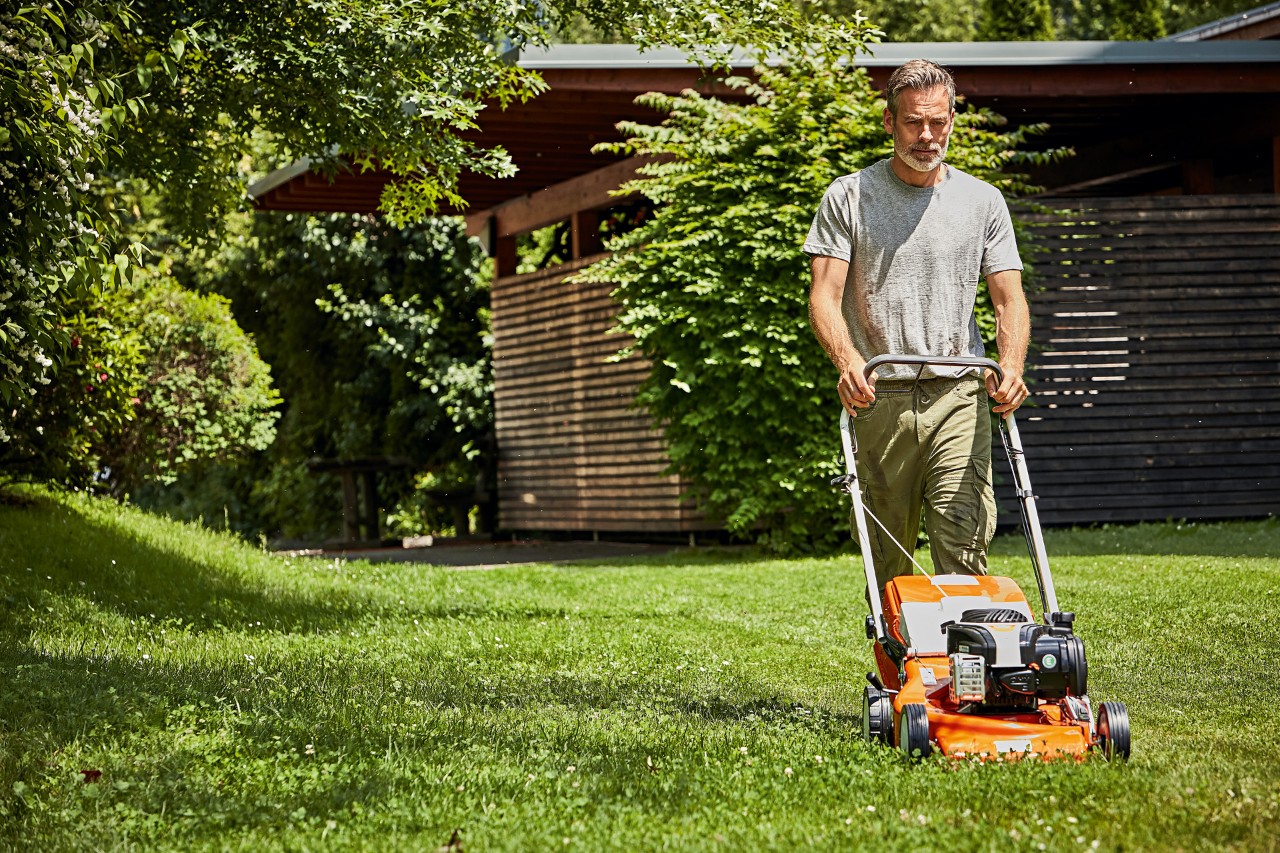  A man correctly mowing the lawn with a STIHL RM 248 petrol-driven lawn mower in front of a garden shed