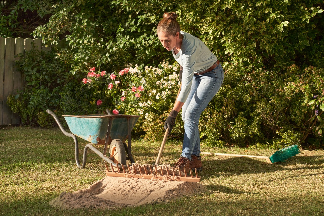 A woman sanding her lawn with a wheelbarrow in the background