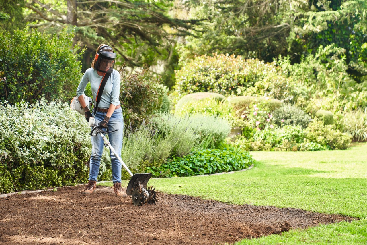 A woman using the STIHL KM 56 RC-E with tiller KombiTool to prepare the soil for rolled turf 