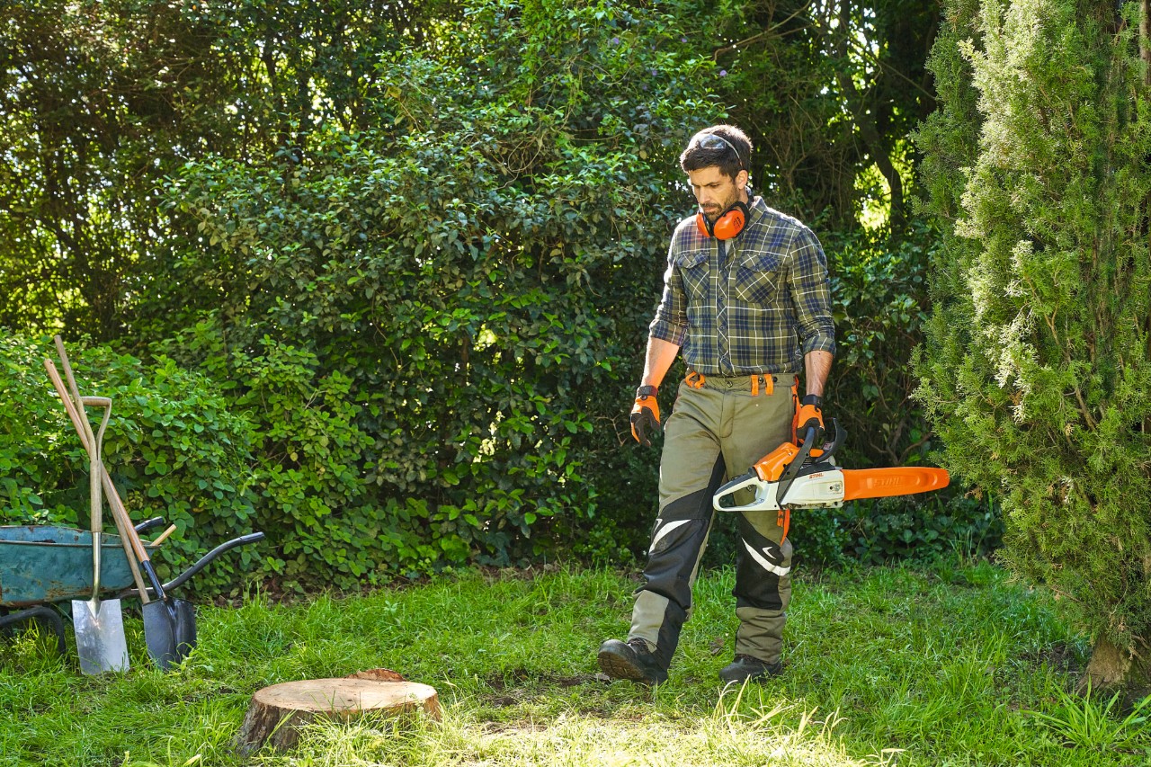 A man wearing protective equipment approaches a tree stump with the STIHL MS 162 chainsaw