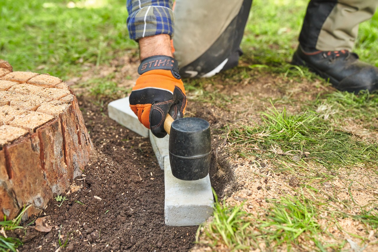Close-up of a person tapping stones into a trench around the tree stump using a rubber mallet 
