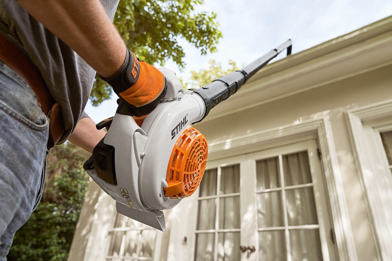 Upward shot of a STIHL gutter cleaning set and leaf blower being used to clean gutters on a white house