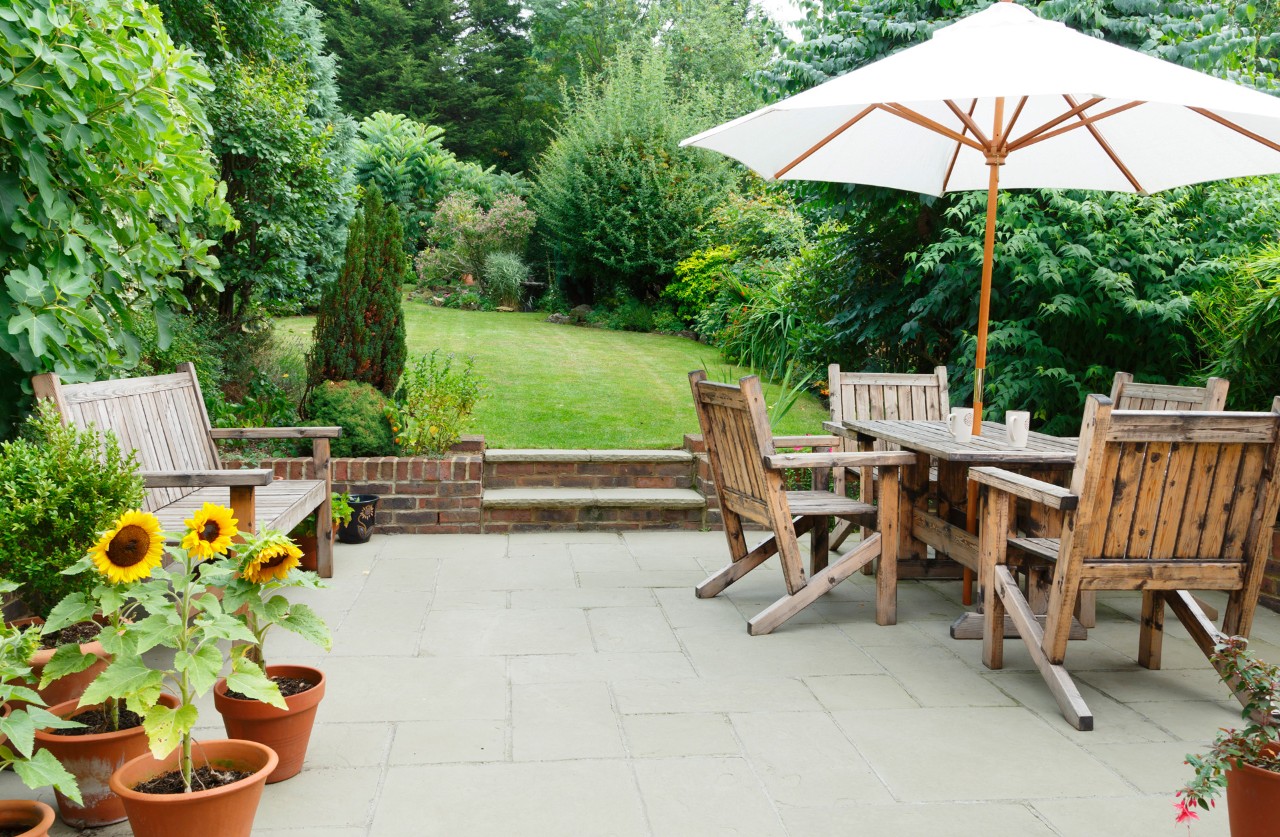 Wooden furniture on a spacious terrace with concrete paving in a large, green garden