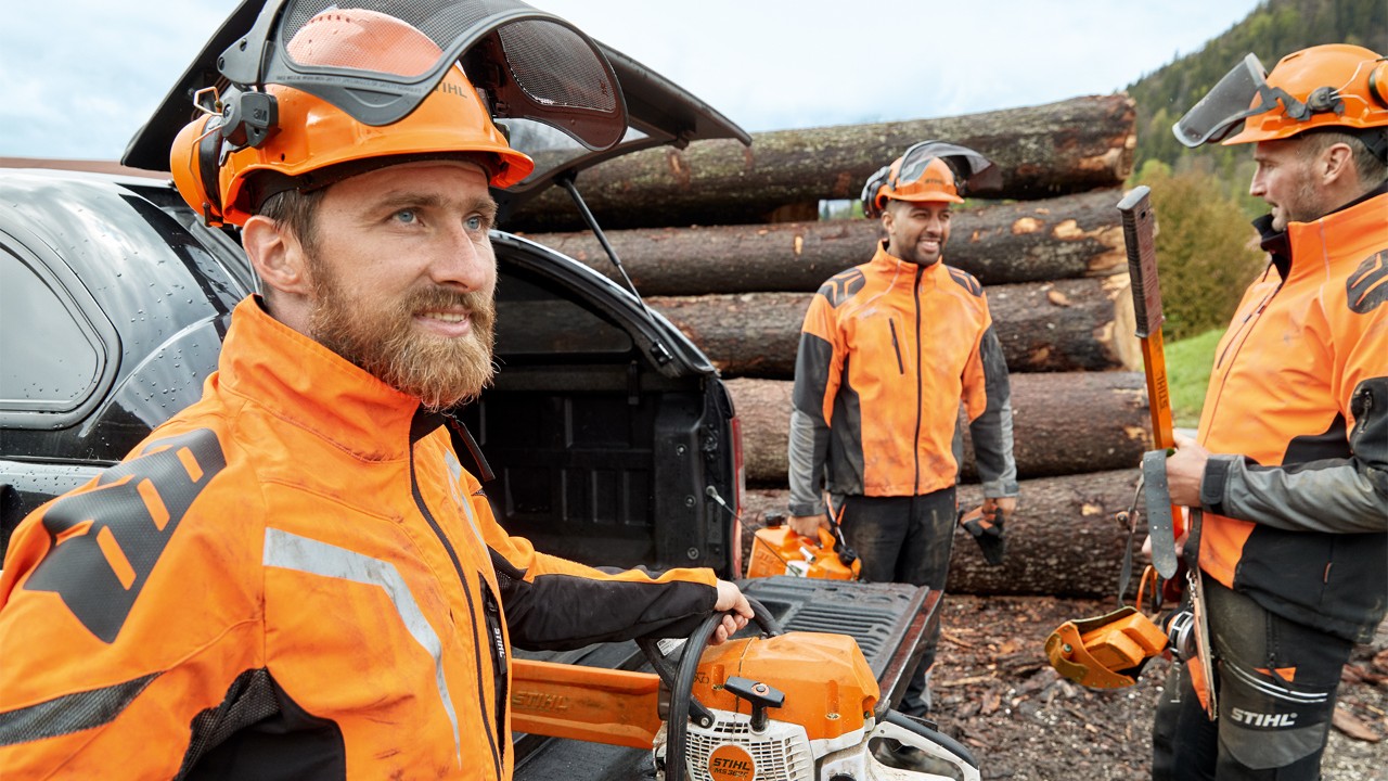 Men wearing protective equipment standing in front of some felled trees