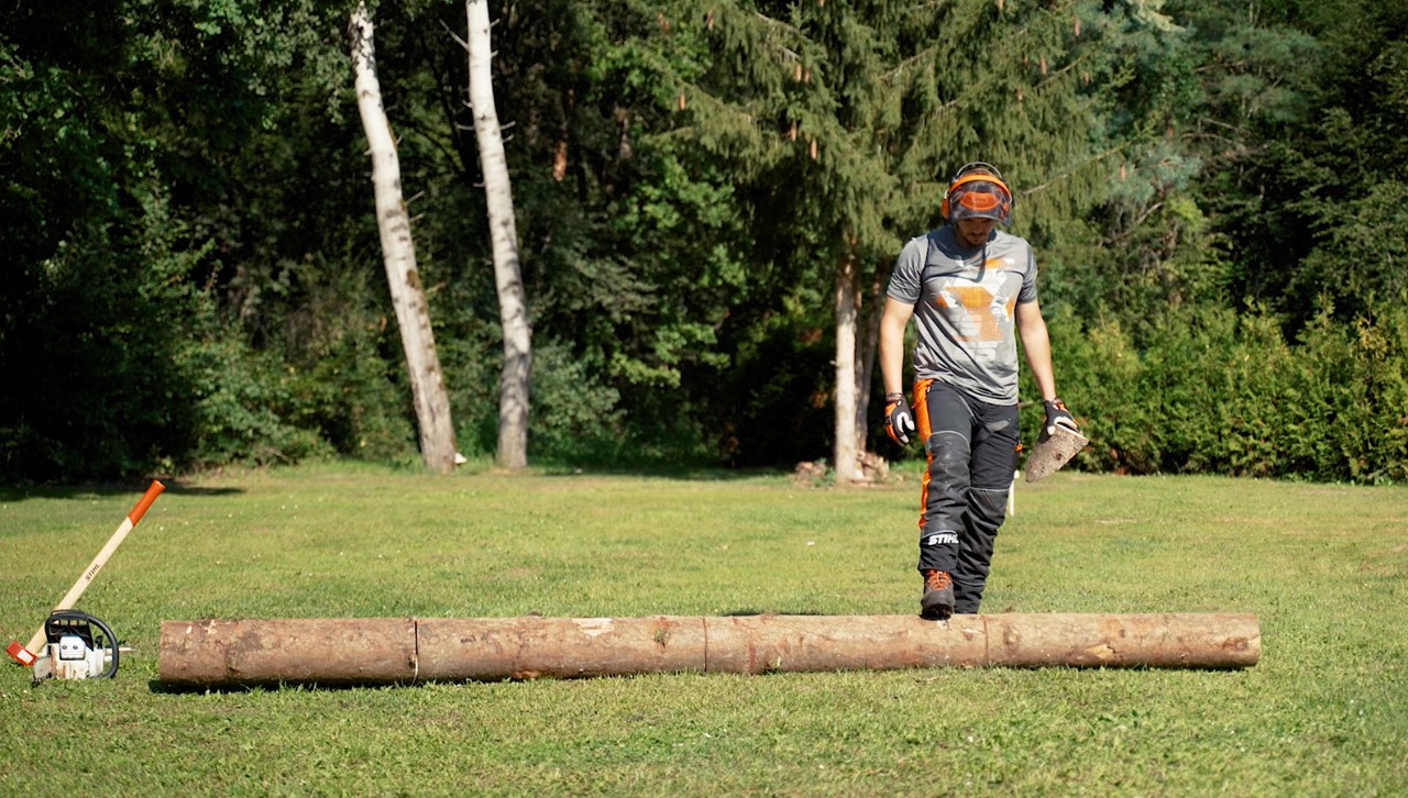 A person turns a tree trunk with his foot to cut firewood