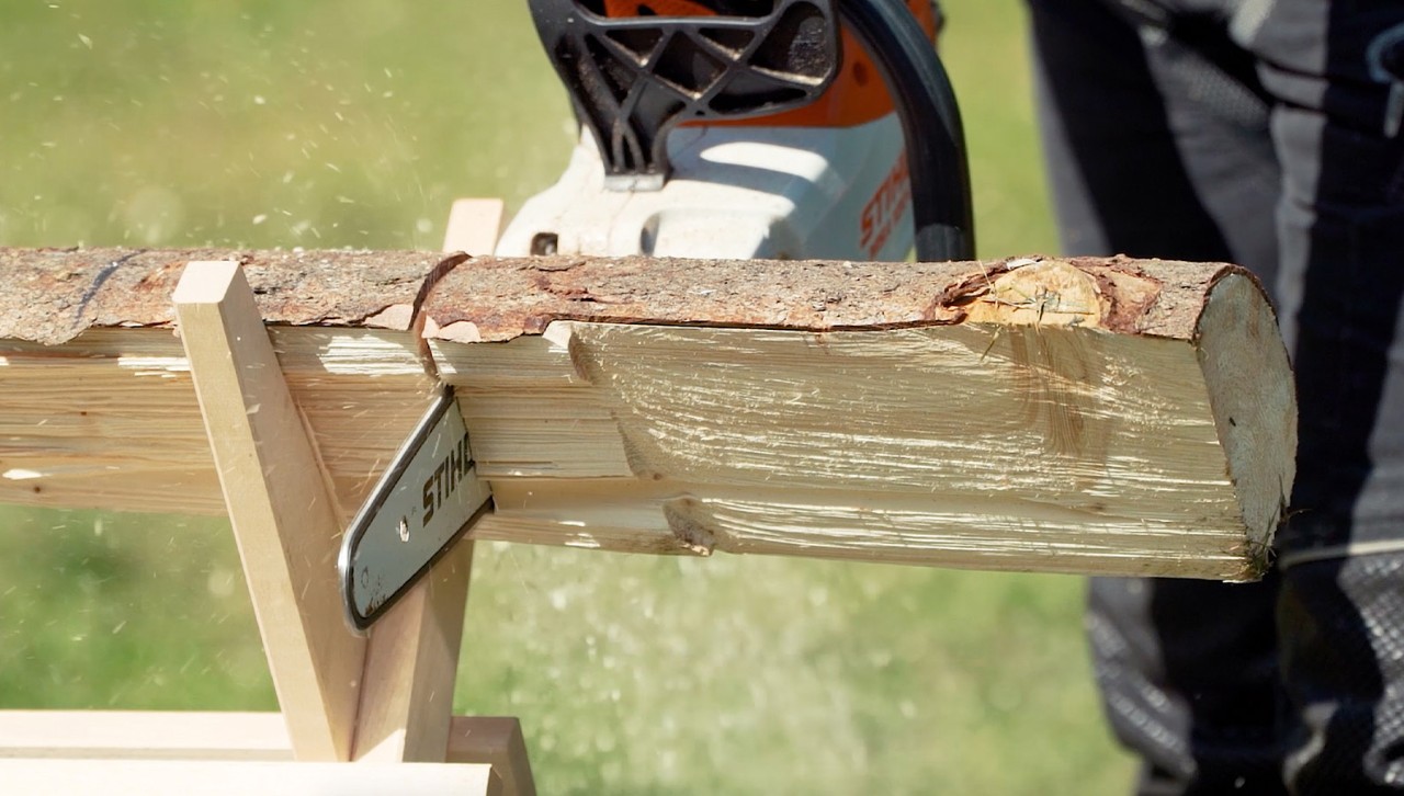 Someone wearing PPE cuts a log on a sawhorse using a STIHL chainsaw MSA 120 C.