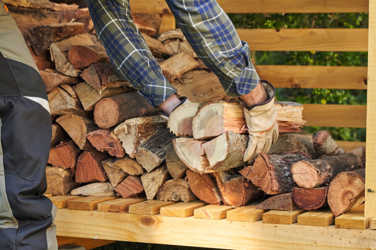 Close-up of a person wearing protective gloves and removing logs from an outdoor log storage shed