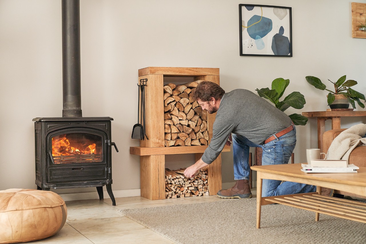 A man removing logs from an indoor DIY log storage rack in a living room to fill the fireplace