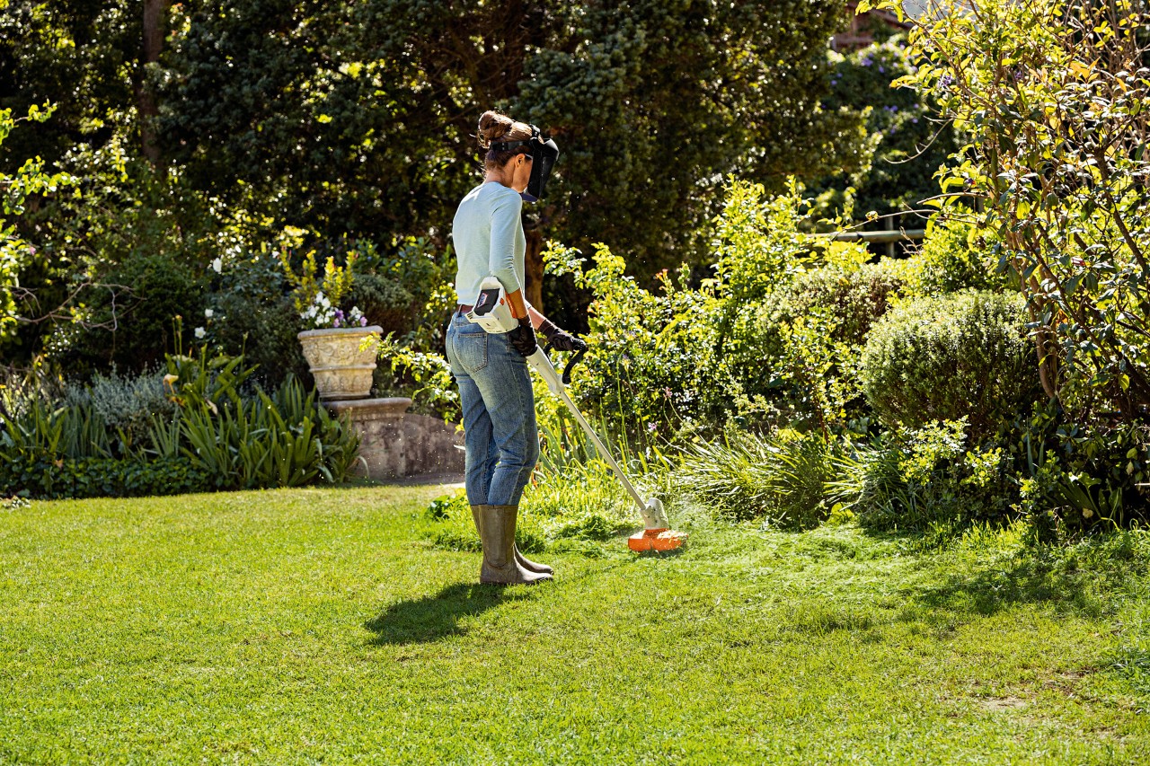A woman mowing long grass on the edge of a property with a STIHL FSA 57 cordless brushcutter