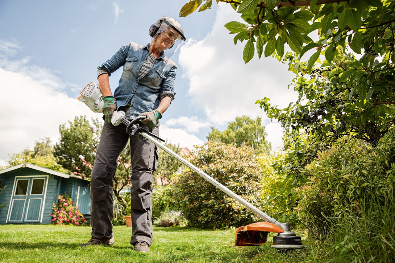Woman wearing face/ear protection trimming a lawn edge with a STHIL FS 58 R petrol brushcutter