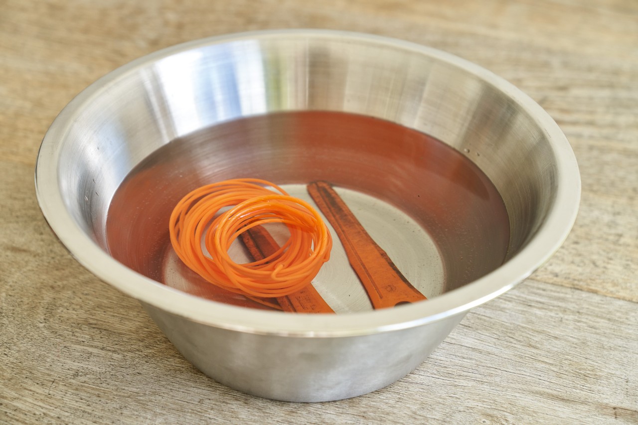 Mowing line and PolyCut blade from a brushcutter in water in a small metal bowl on a wooden floor