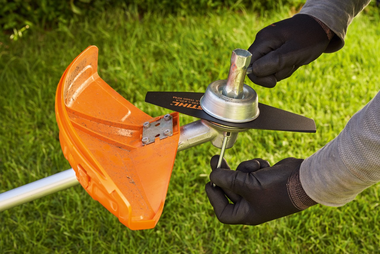 A person wearing protective gloves checking the metal cutting tool of a brushcutter