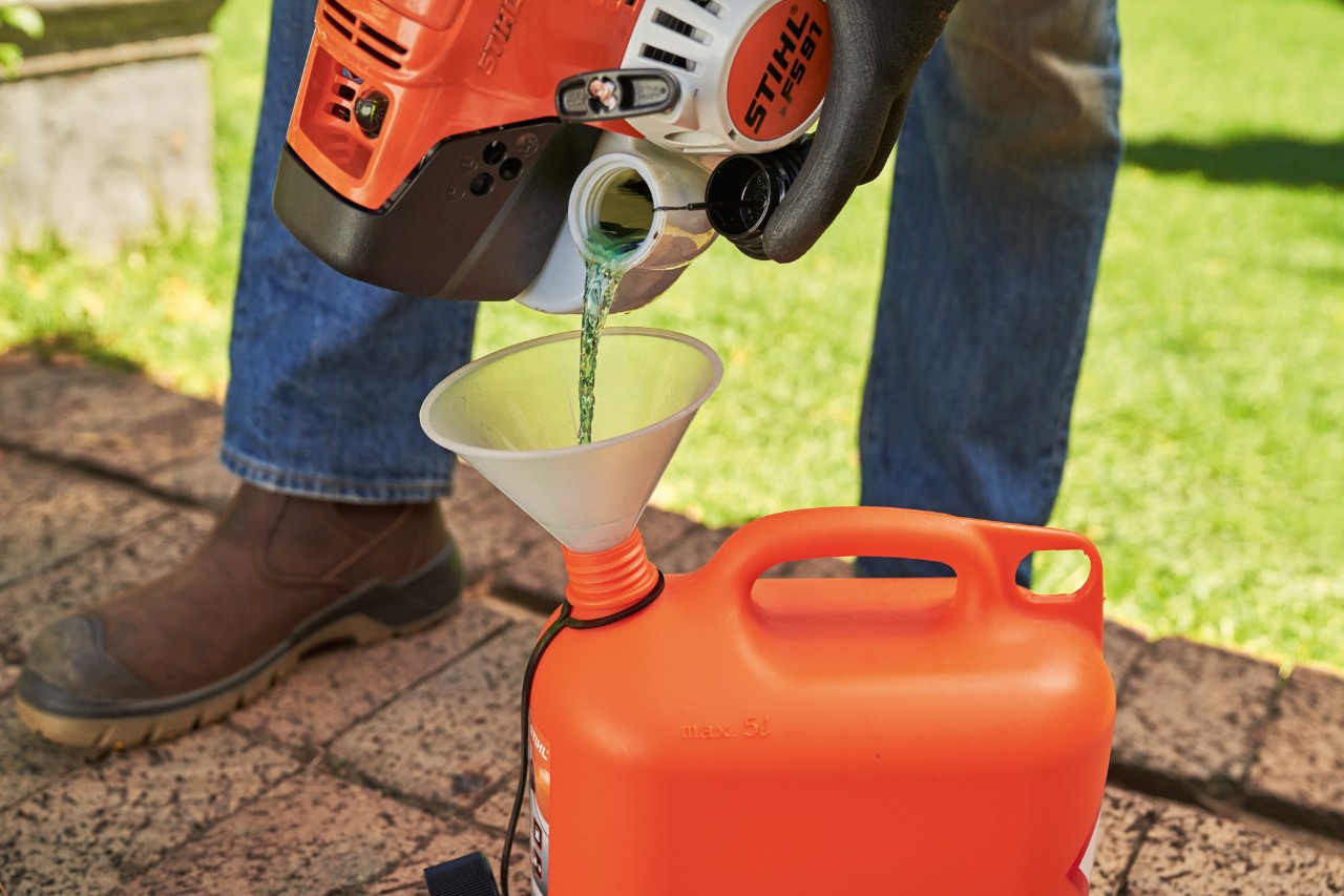 Emptying the tank of a brushcutter into a canister using a funnel