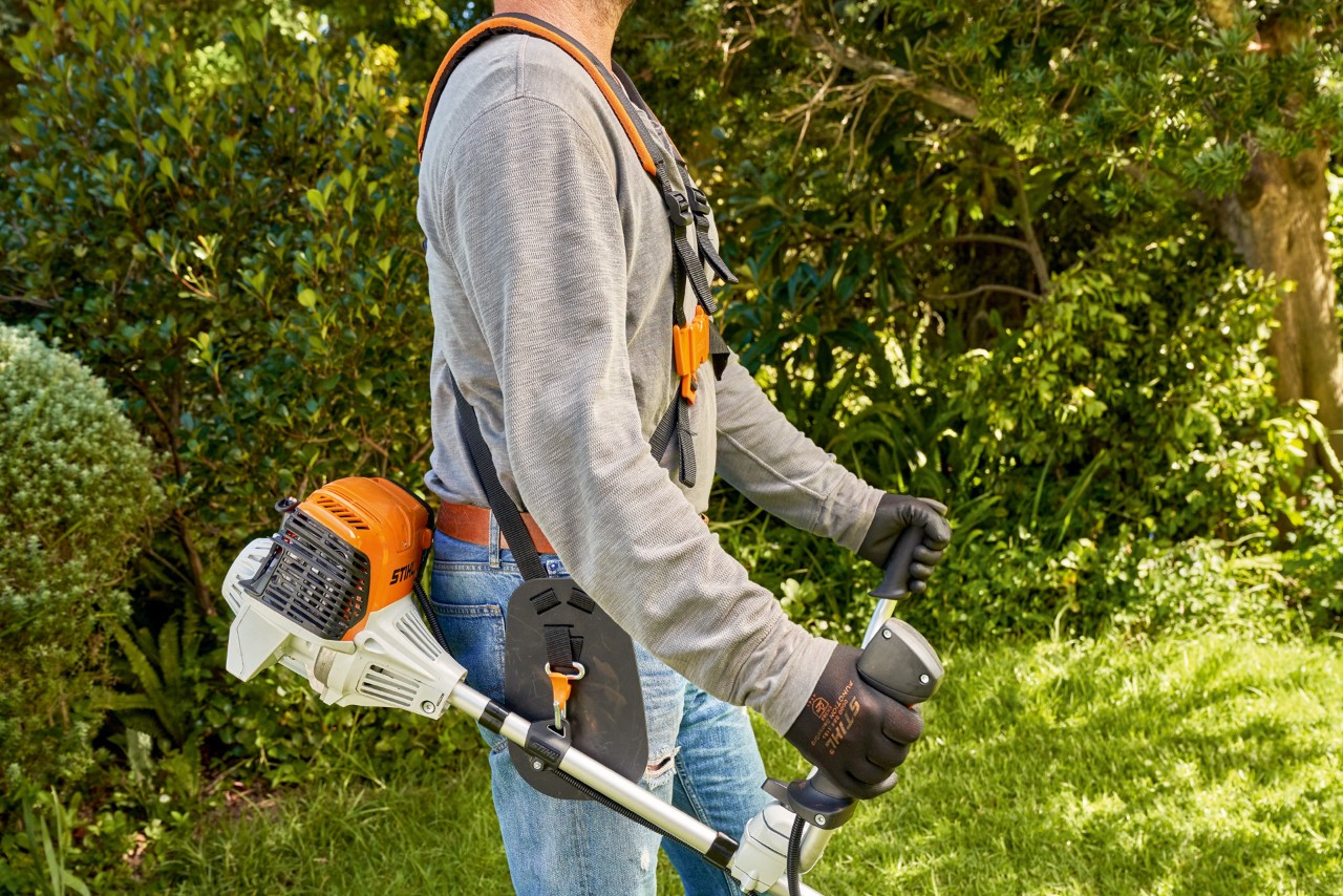 A man picking up a STIHL FS 91 petrol brushcutter from the ground to start mowing 