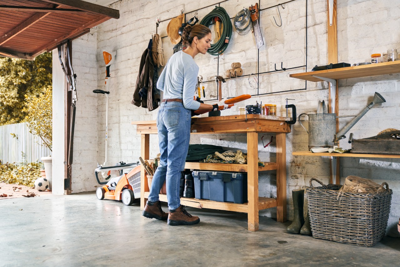 Woman wearing protective gloves maintaining a STIHL HSA 56 battery hedge trimmer on a workbench