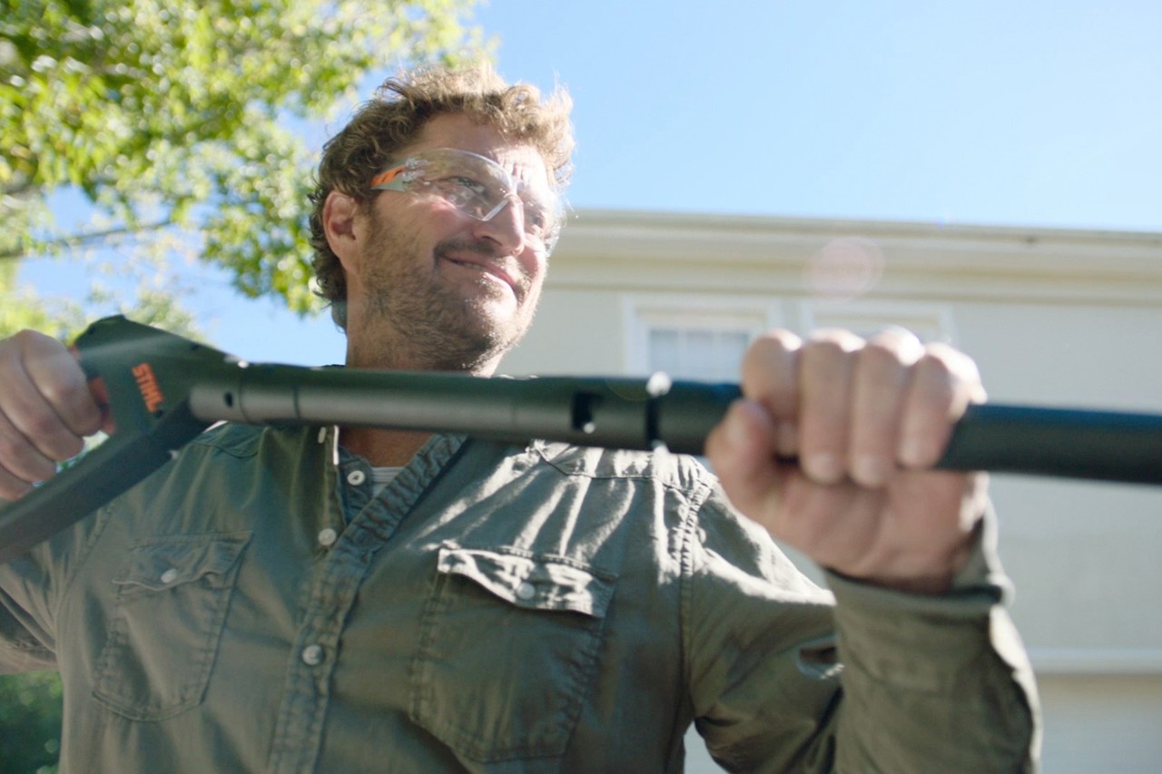 A man wearing safety glasses holding the STIHL RE 130 PLUS high-pressure cleaner for wet blasting, with a house behind  