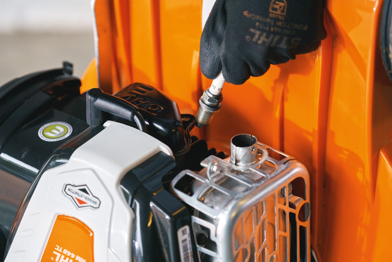 Close-up of someone removing a spark plug from a lawn mower that has been tipped upright