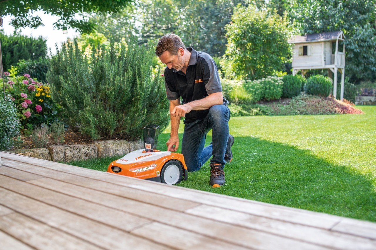 A STIHL dealer uses the control panel of a STIHL iMOW® 422 robotic mower in a garden