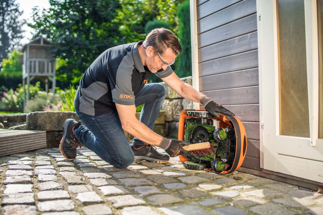 A man uses a brush to clean the underside of a STIHL iMOW® 422 robot lawn mower 