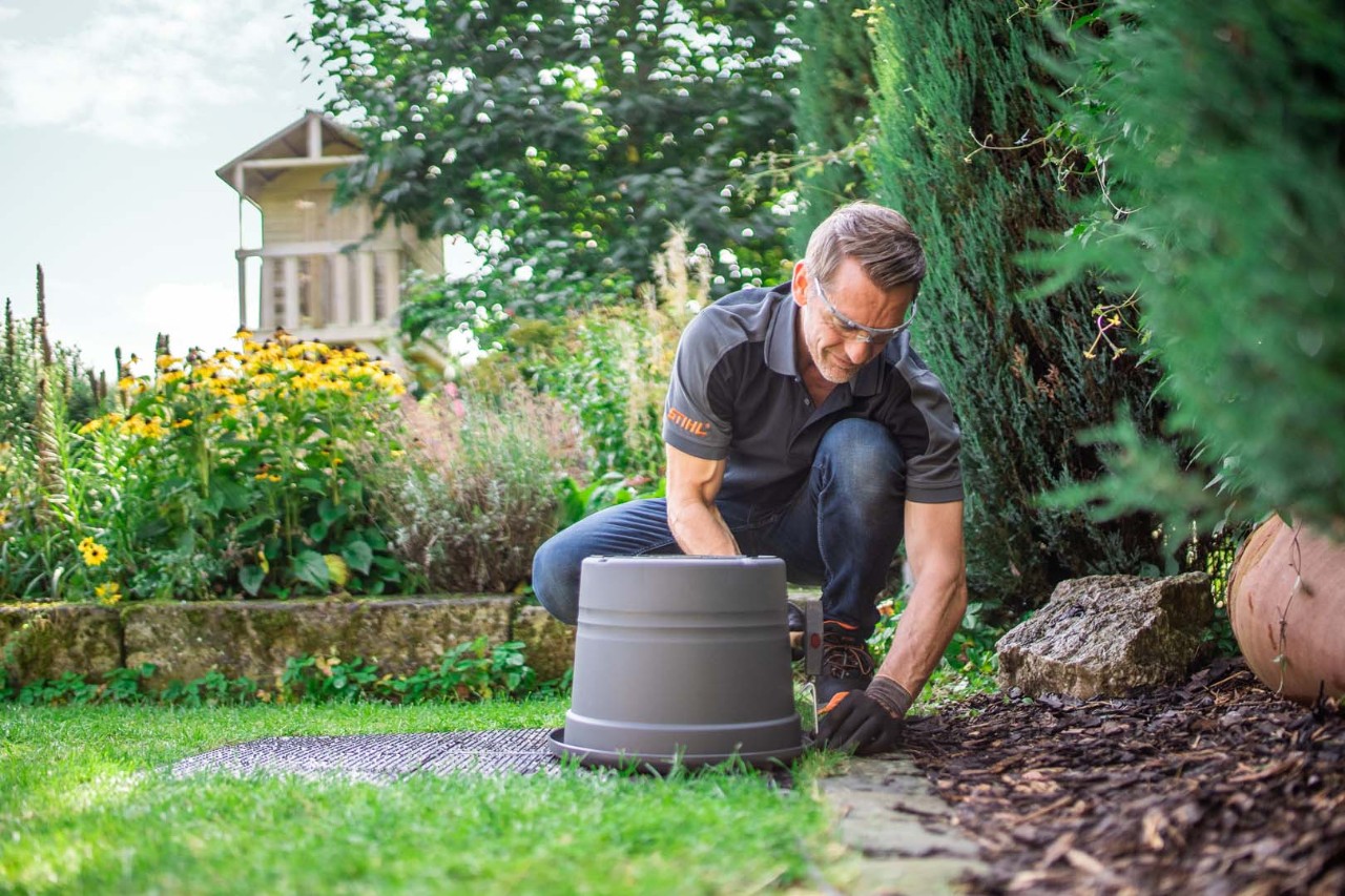 A man wearing safety glasses secures a bucket over a STIHL iMOW® robot mower docking station